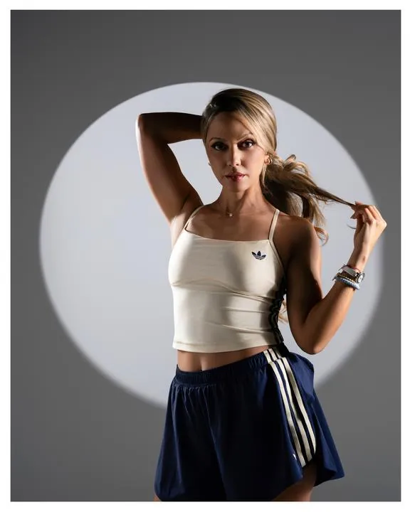 Modelo con top blanco y short adidas posando frente a un círculo de luz