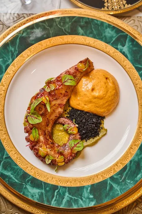 Pulpo con puré y arroz negro en plato verde con borde dorado