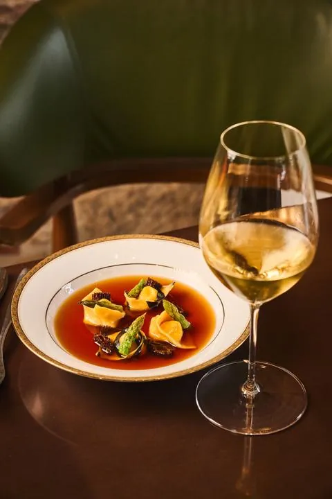 Plato de pasta rellena en consomé junto a una copa de vino blanco
